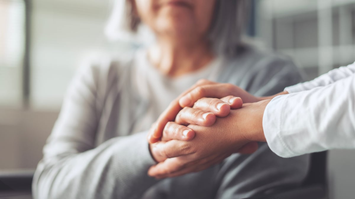 Hands holding an elderly woman's hands, representing compassionate care and trust